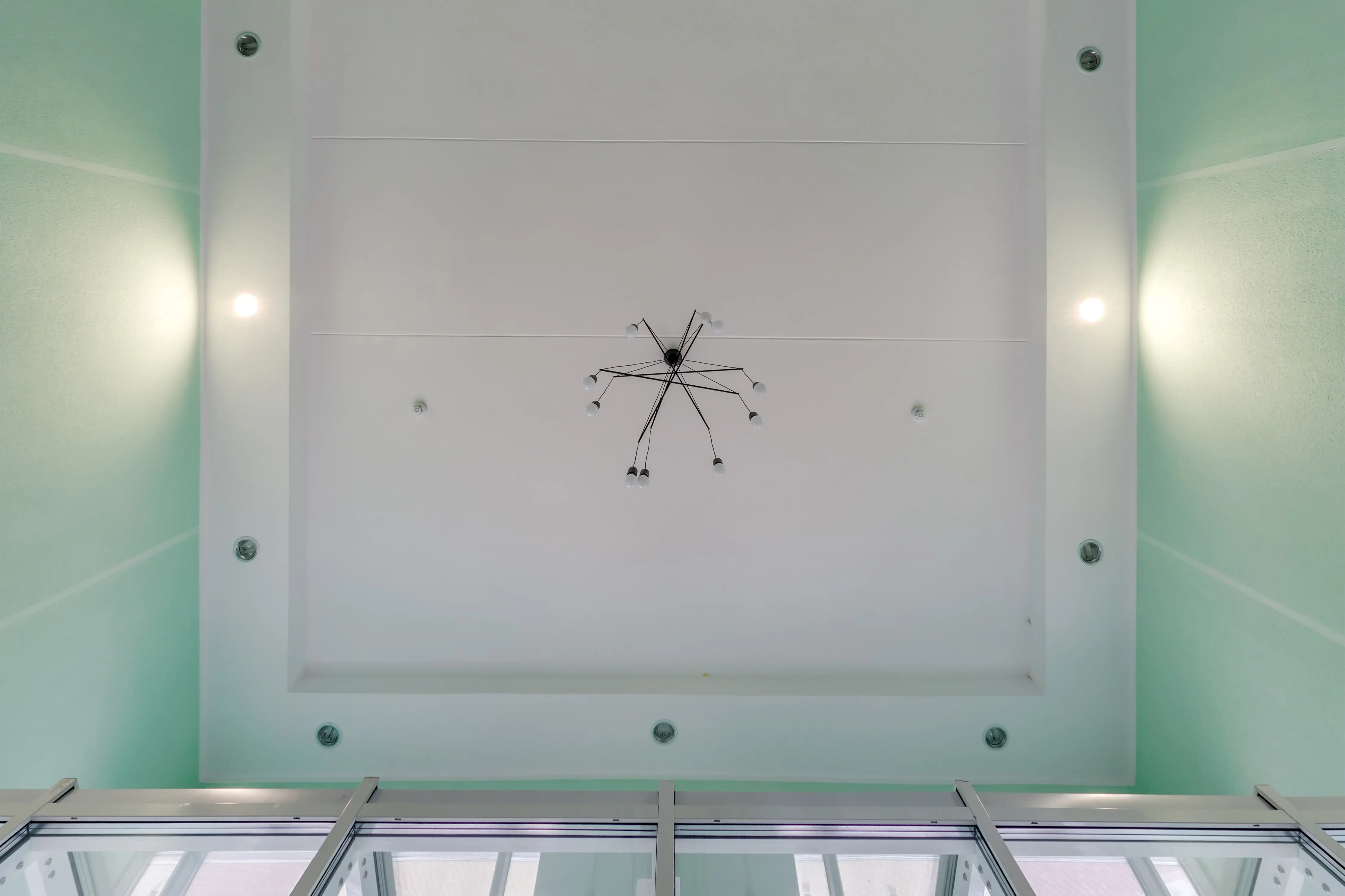 Abgehängte Decke mit Halogen-Spotlampen und Trockenbaukonstruktion in einem leeren Raum in einer Wohnung oder einem Haus; weiße, komplex geformte Spanndecke.